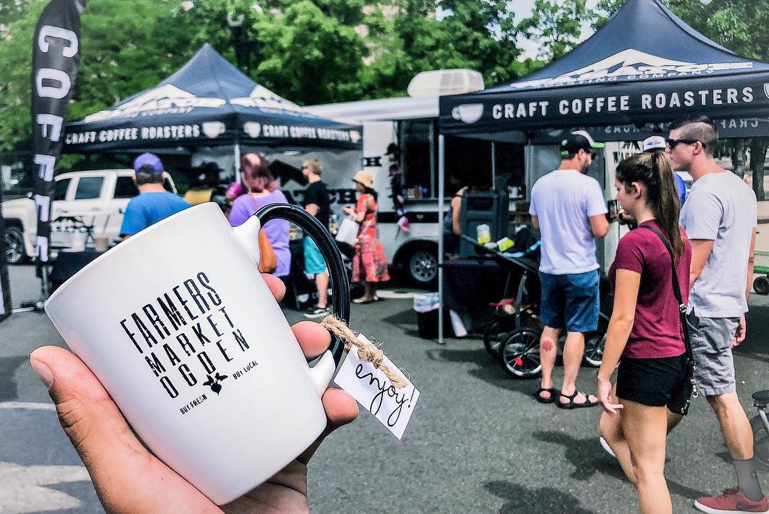 an image of a farmers market coffee mug being held up in front of Wasatch Roasting Compan's booth
